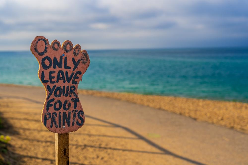 Skilt på strand formet som en fod med teksten "Only leave your foot prints" 
